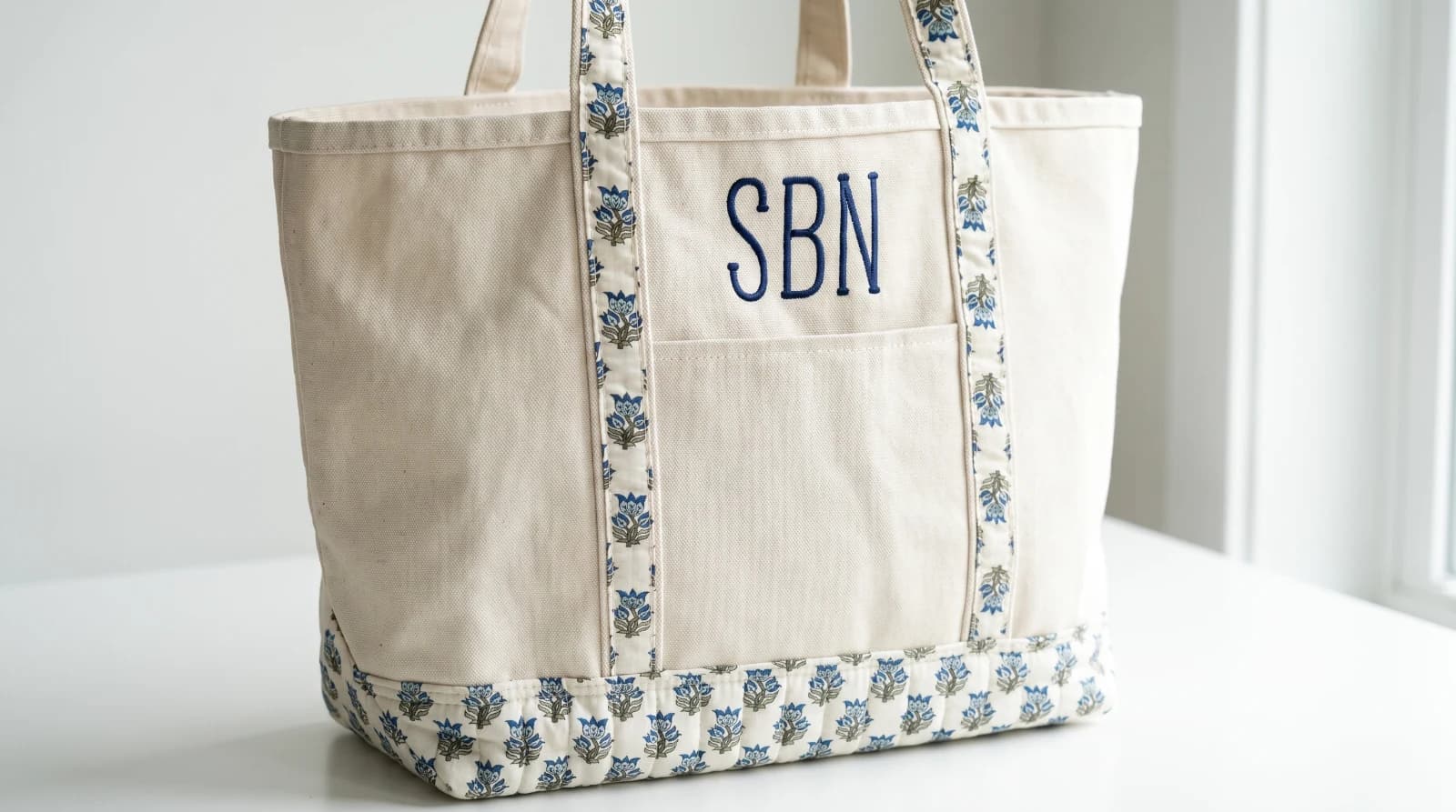 A stitched piece from Four Burners Embroidery: a navy SBN monogram embroidered on a cream canvas tote with a blue floral trim