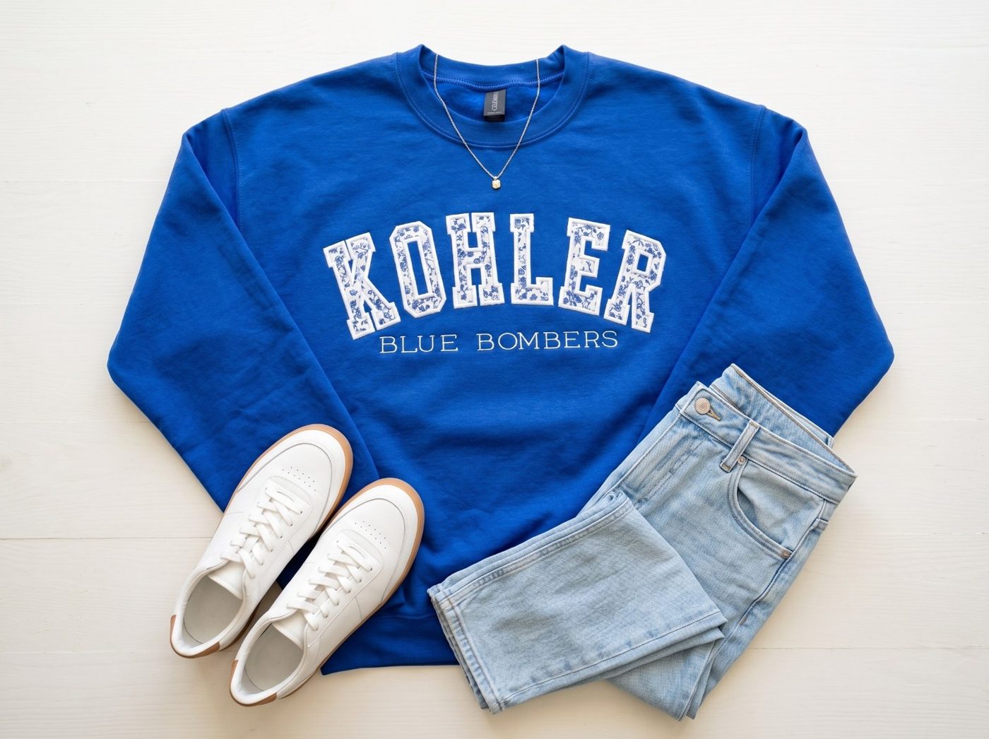 The same blue appliqué crewneck as a styled flat-lay with jeans and sneakers